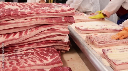 Pan right, workers rub seasoning on raw meat