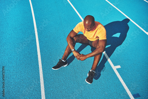 Smiling young runner resting on a running track after training