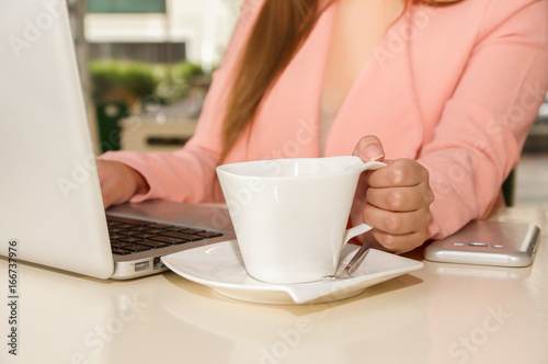 Close up of businesswoman hand working and holding with one hand a cup of coffe. Business concept