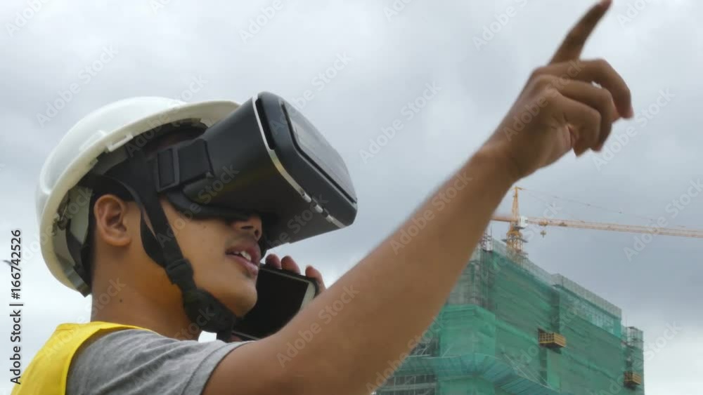 Medium of multicultural ethnic construction worker/tradesman/architect/designer uses a VR headset while communicating with a colleague on his smart phone at a building project