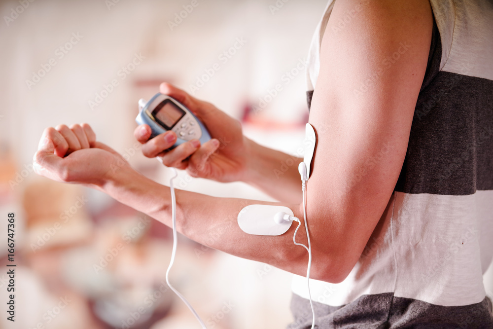 Close-up of a man holding an electrode machine in his hand and with electrostimulator electrodes in the arm of a fitness young man in a blurred background Close-up of a man holding an electrode machine in his hand and with electrostimulator electrodes in the arm of a fitness young man in a blurred background