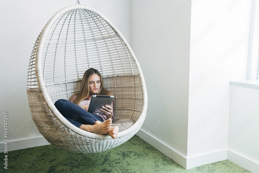 Woman in hanging wicker chair reading on a tablet computer Stock Photo |  Adobe Stock