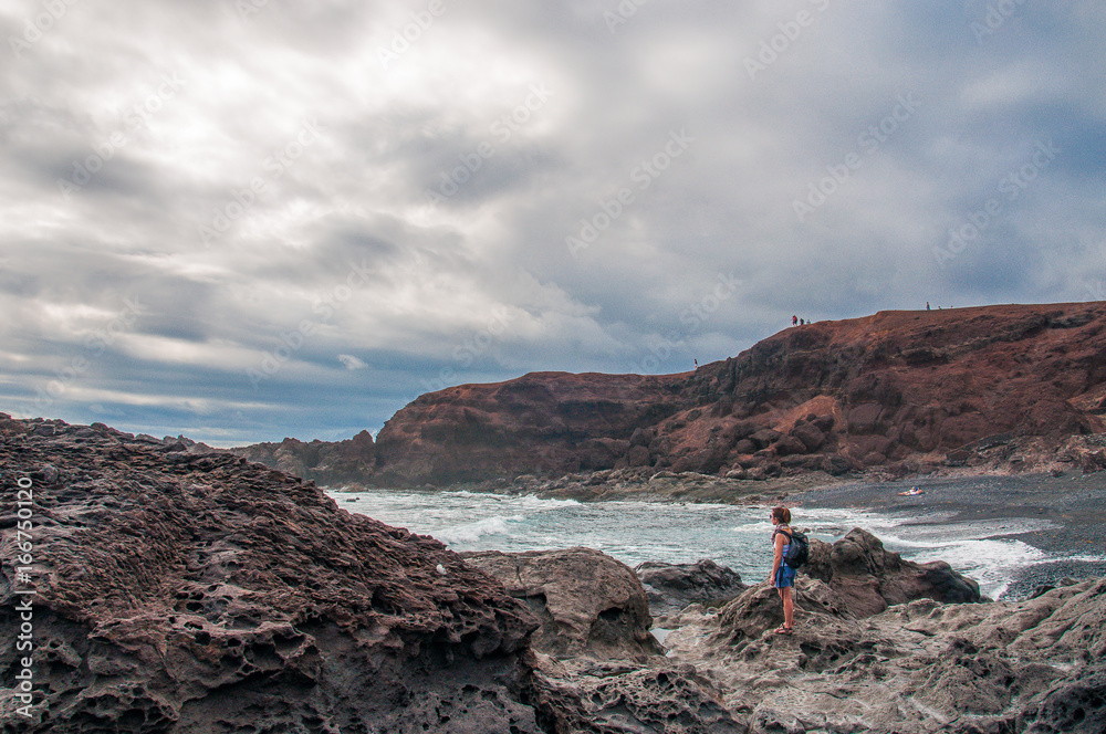 Girl watching cloudy sky on rocky beach, Charco de los Clicos, Lanzarote, Canary Islands