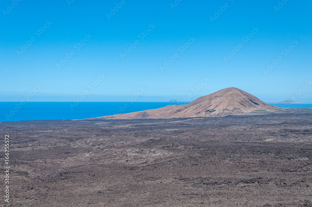 Volcanic cone along Lanzarote coastline surrounded by ancient basaltic lava flows, Lanzarote, Canary Islands