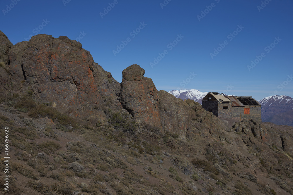 Derelict mountain hut, Refugio Alemana, in the mountainous landscape of Parque Yerba Loca set in a glacial valley close to Santiago, capital of Chile. Santiago in the distance under a layer of smog. Derelict mountain hut, Refugio Alemana, in the mountainous landscape of Parque Yerba Loca set in a glacial valley close to Santiago, capital of Chile. Santiago in the distance under a layer of smog.