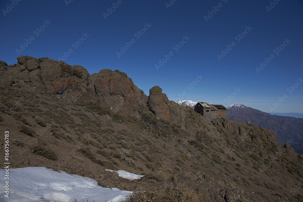 Derelict mountain hut, Refugio Alemana, in the mountainous landscape of Parque Yerba Loca set in a glacial valley close to Santiago, capital of Chile. Santiago in the distance under a layer of smog.