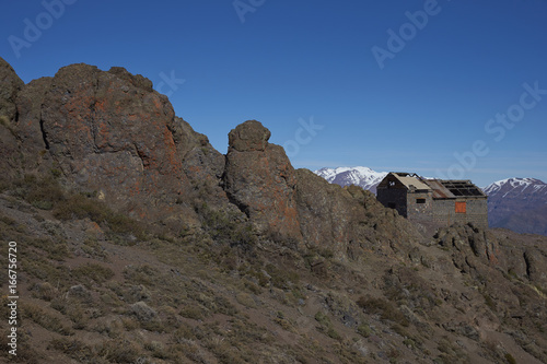 Derelict mountain hut, Refugio Alemana, in the mountainous landscape of Parque Yerba Loca set in a glacial valley close to Santiago, capital of Chile. Santiago in the distance under a layer of smog.