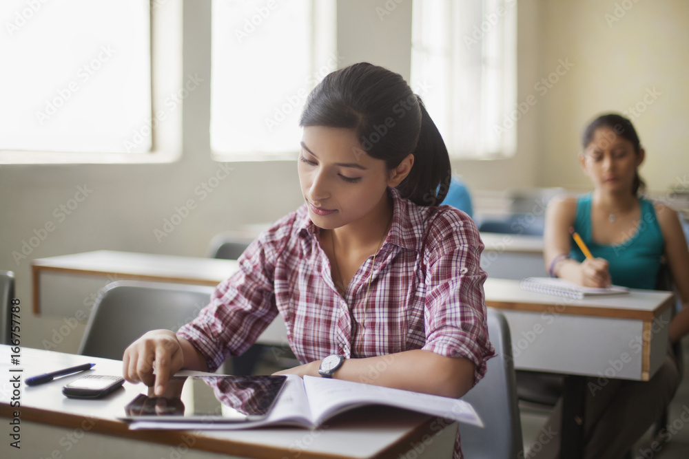 Teenage girl using digital tablet at desk in classroom Teenage girl using digital tablet at desk in classroom