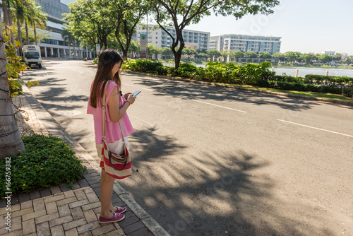 Young woman checking smart phone outdoors in sunny morning photo