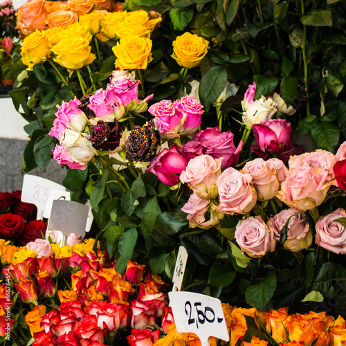 Flower arragements and bouquets of yellow, pink, red and orange roses for sale at florist stand with deep green leaves photo