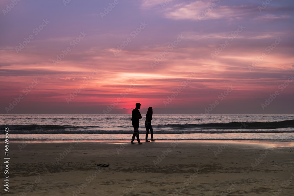 A couple walking by the beach when sundown with beautiful twilight in the background. Image contain motion blur and grains due to low light ambiance and movement.