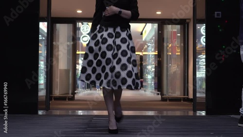 A beautiful woman in a dress comes out of the store through a sliding glass door