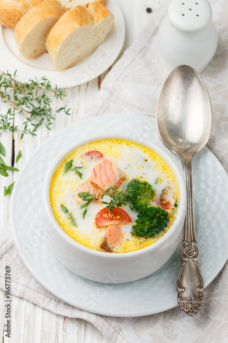 Salmon creamy soup with vegetables - potatoes, carrots, tomatoes and broccoli in a white bowl on bright wooden table