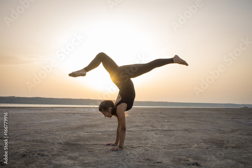 Young fit woman training yoga poses in desert during the sunset or sunrise, female in black sportswear do stretching exercises 