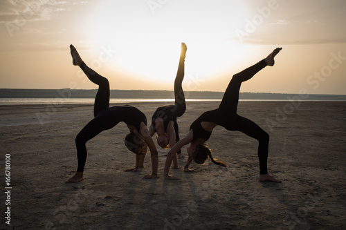 young women practicing yoga poses and asanas. Partner yoga, acrobatic yoga. Yoga class in black wear training in desert during sunset 