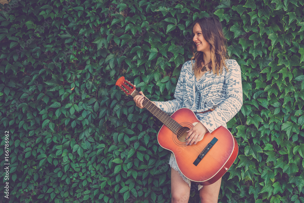 Female playing guitar against green leaf wall background