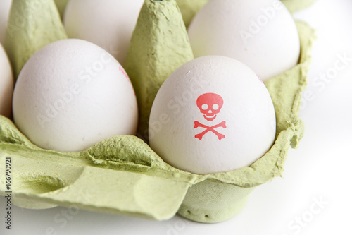 Eggs in a green paper package with one of the eggs painted with a red poisonous risk symbol skull and bones. Image concept for food contamination. photo