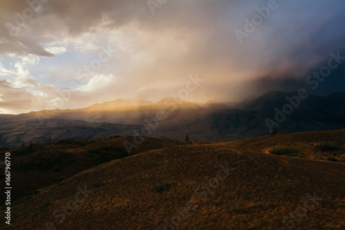 Sunset, bright sunlight in a dusty cloud, travel on the mountain valley, a landscape
