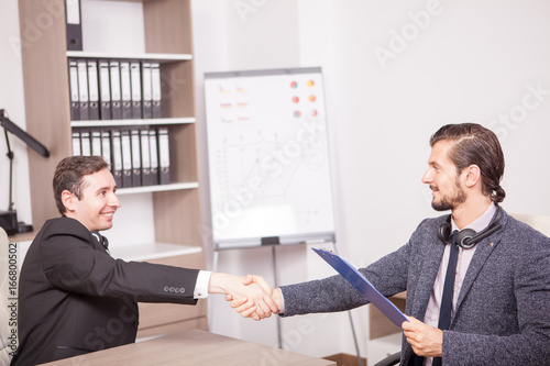 Business partners shaking hands in the office. Two businessman in formal suits shaking hands in corporate office eviroment photo