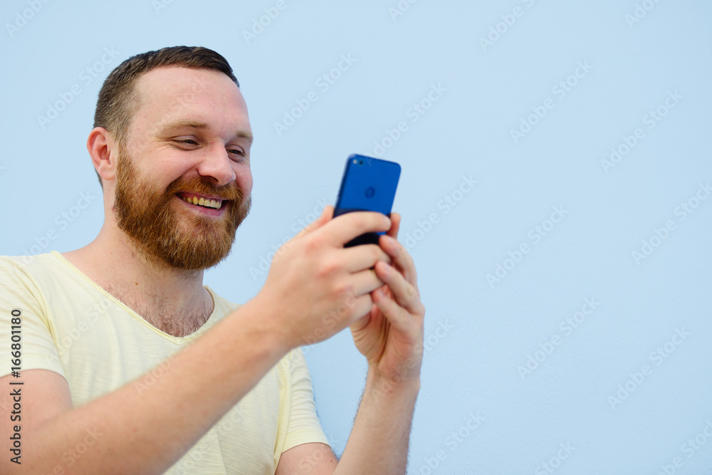 man with a red beard looks into the phone with surprise and ecstasy a bright summer photo on a blue background man with a red beard looks into the phone with surprise and ecstasy a bright summer photo on a blue background