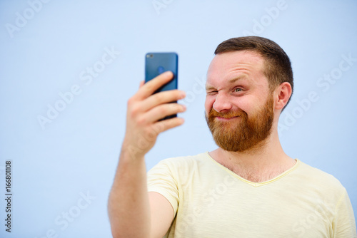 Cheerful bearded Man winks at the phone, suitable for advertising, on a blue background