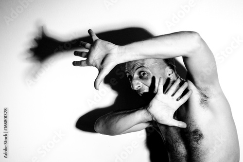 Frightened and alarmed man, very afraid fugitive, terrified and trapped clandestine man in full light with big shadow, protecting himself with his hands, nightmare scene photo