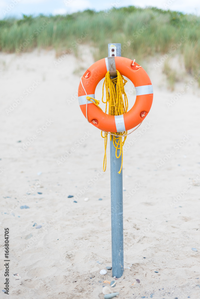 Orange lifebuoy in foreground. sand in background. Bright sunny day. Holidays at beach. Beautiful seascape. Equipment for rescue of people. Service for lifesaving.