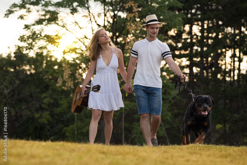 Young couple in love with guitar and dog rottweiler in the nature