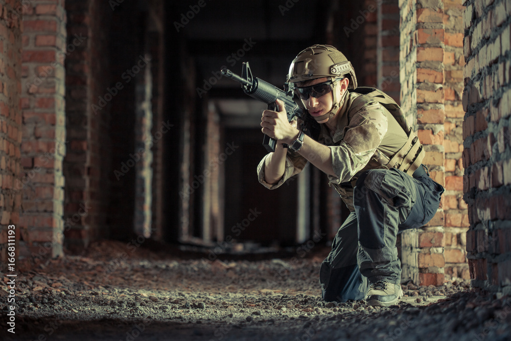 Fototapeta premium airsoft soldier with a rifle playing strikeball In brick building