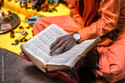 Fototapeta Old sadhu hand wearing hand watch pointing at line of holy book Varanasi, India