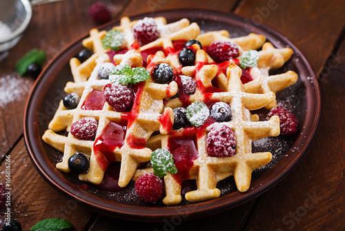 Belgium waffles with raspberries and syrup on a plate.