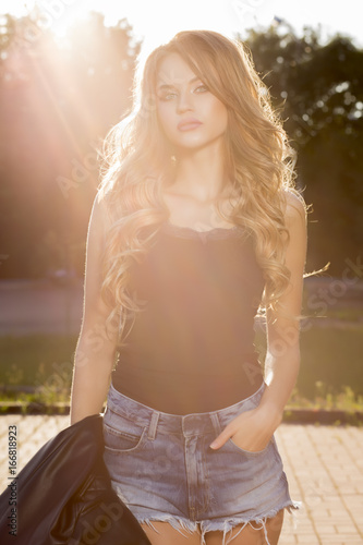 Glamor young model with lush wave hair posing in rays of sun