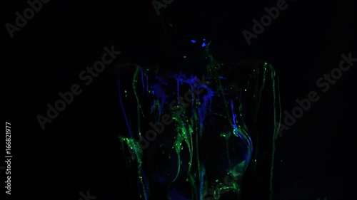 A girl with a bare breast smeared with fluorescent paint posing in the dark posing in the dark photo