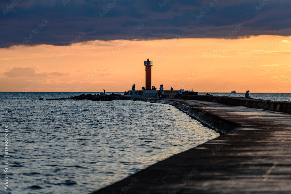 people enjoying sunset on the breakwater in the sea with lighthouse