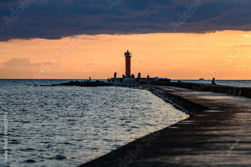 people enjoying sunset on the breakwater in the sea with lighthouse