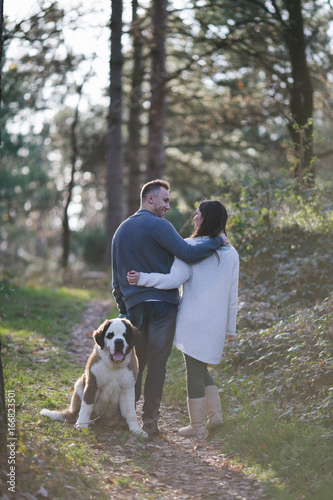 Young couple enjoying nature outdoors together with their Saint Bernard puppy. 