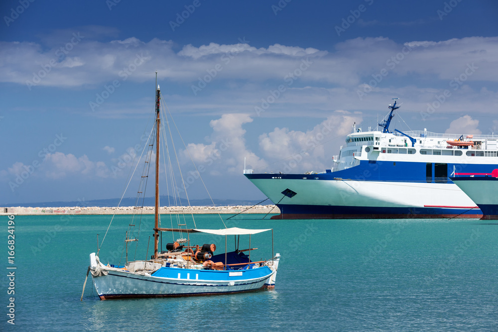A small yacht stands in the port of Zakynthos on the background of a large sailing vessel.