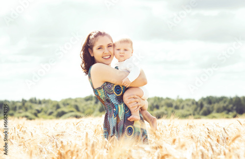 Beautiful woman holding baby. Mother and son walking in a meadow at summer.