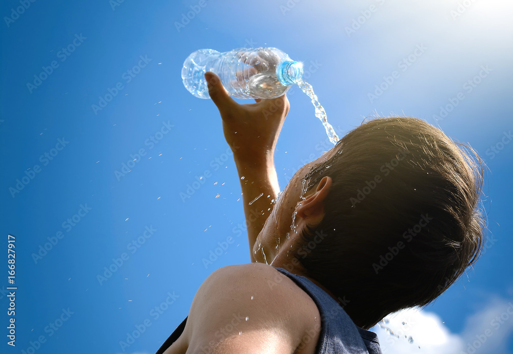 Young man splashing and pouring fresh water from a bottle on his face ...