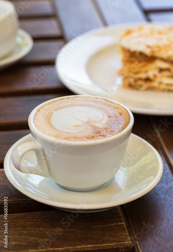 Napoleon cake, cappuccino coffee on a wooden table on the veranda in the cafe, in the garden