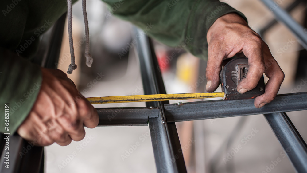 Worker measuring steel with measuring tape