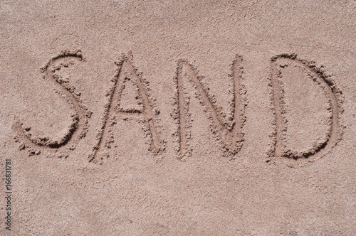 Handwritten word "SAND" on brown sand on the beach in sunny day