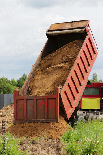 Construction truck unloads sand at the site of repair where laying the pipeline with water. Yellow empty advertising awning on the cab