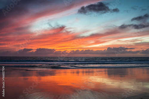 Dramatic red glowing sunset on the beach with water reflections.