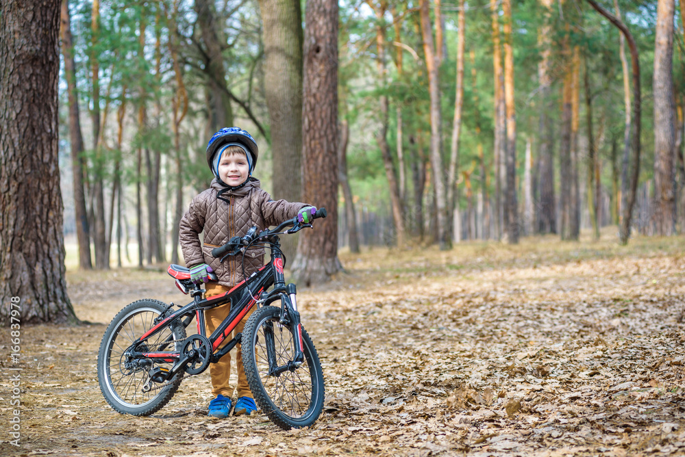 Naklejka premium Happy kid boy of 3 or 5 years having fun in autumn forest with a bicycle on beautiful fall day. Active child wearing bike helmet. Safety, sports, leisure with kids concept.