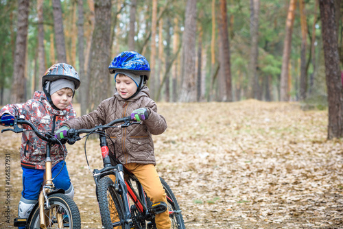 Two little siblings having fun on bikes in autumn or spring forest. Selective focus on boy.