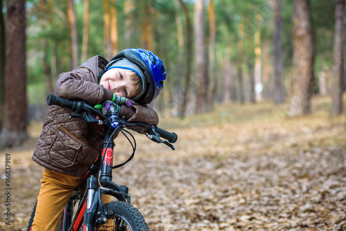 Happy kid boy of 3 or 5 years having fun in autumn forest with a bicycle on beautiful fall day. Active child wearing bike helmet. Safety, sports, leisure with kids concept.