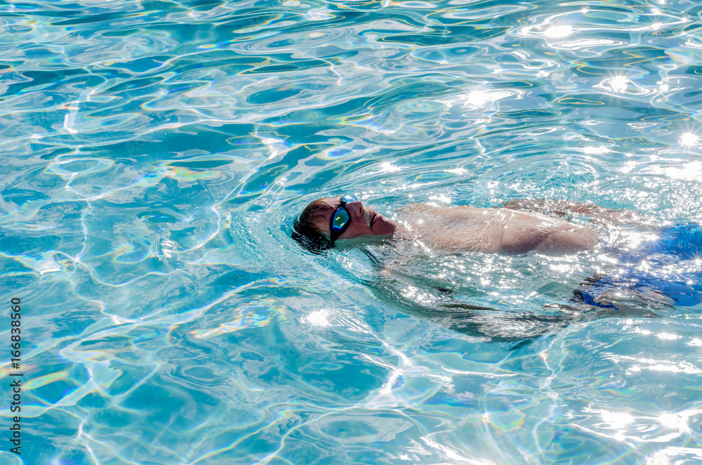 Mature male swimming in a pool, doing backstrokes 