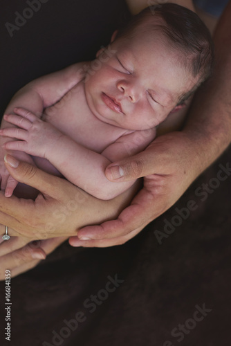 Parents hands hold small baby