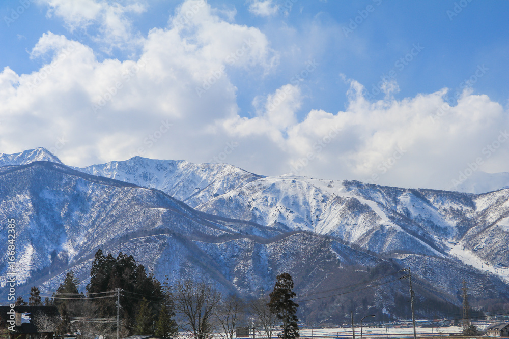 Hakuba mountain range  and  Hakuba village houses  in the winter with snow on the mountain and blue sky and clouds background in Hakuba  Nagano Japan.